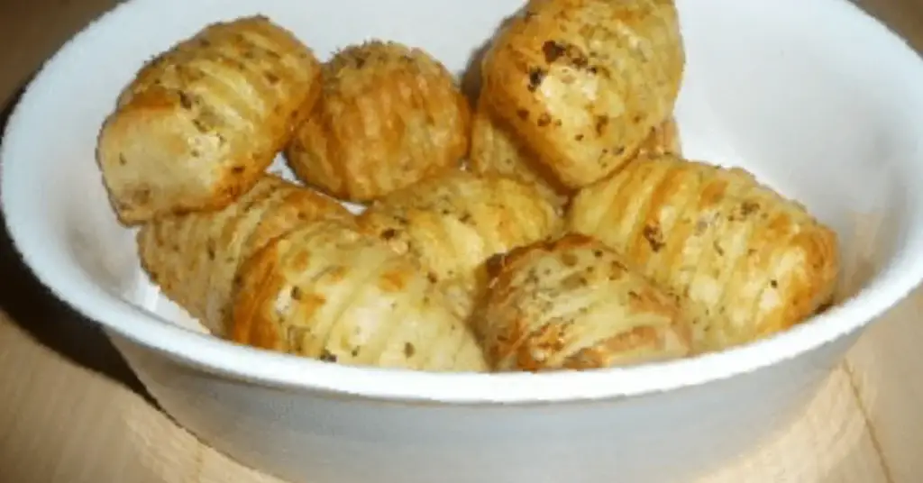 Crispy hasselback potatoes seasoned with herbs and served in a white bowl.