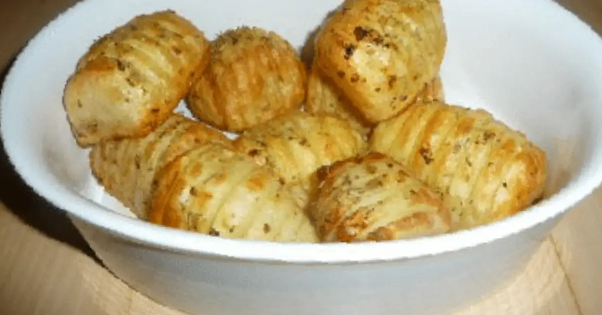 Crispy hasselback potatoes seasoned with herbs and served in a white bowl.