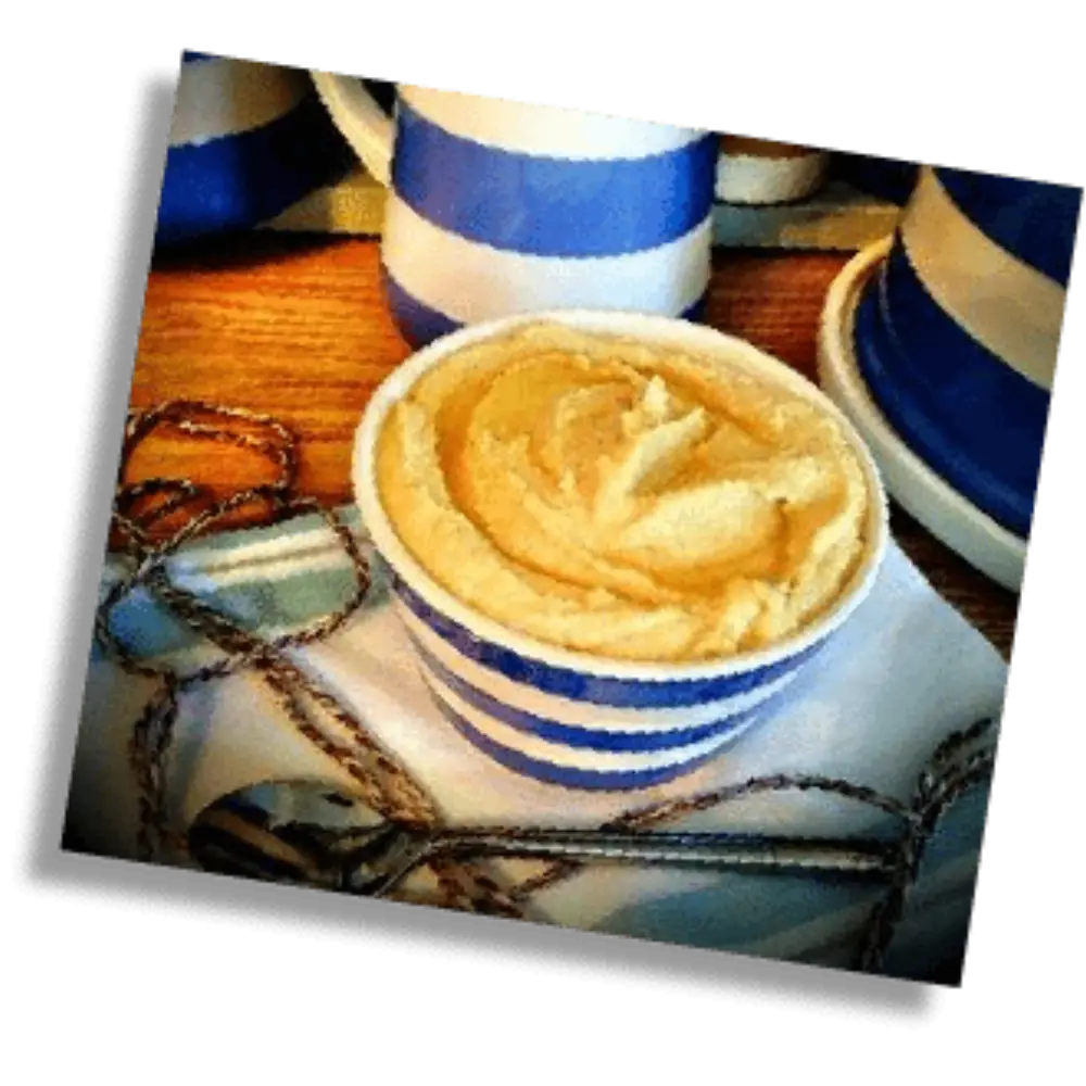 Small bowl of creamy hummus served in blue and white striped tableware with matching dishes in the background.