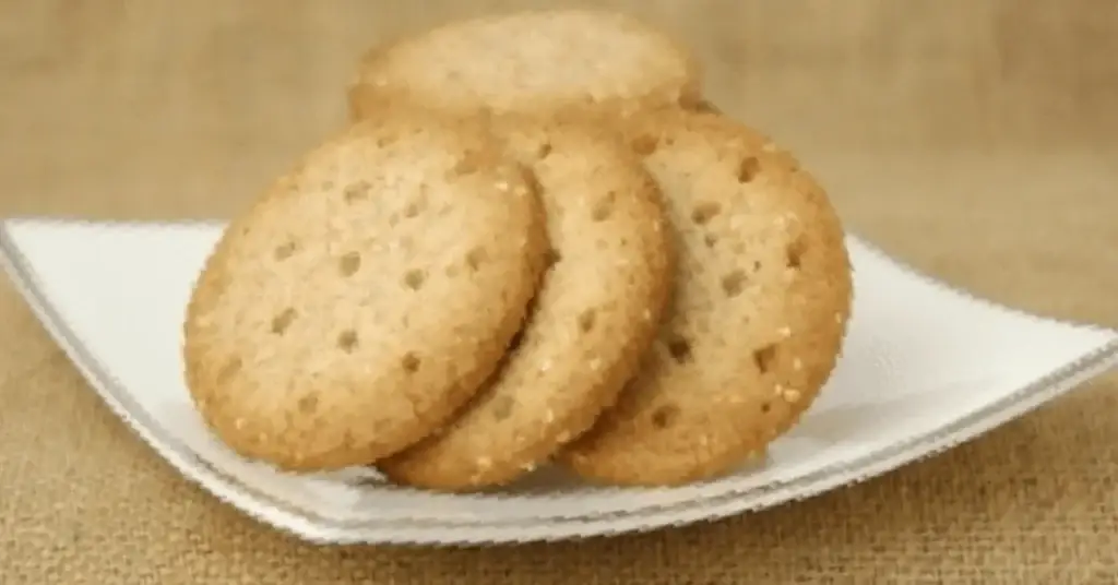 Golden savoury crackers stacked on a white plate against a rustic hessian background.