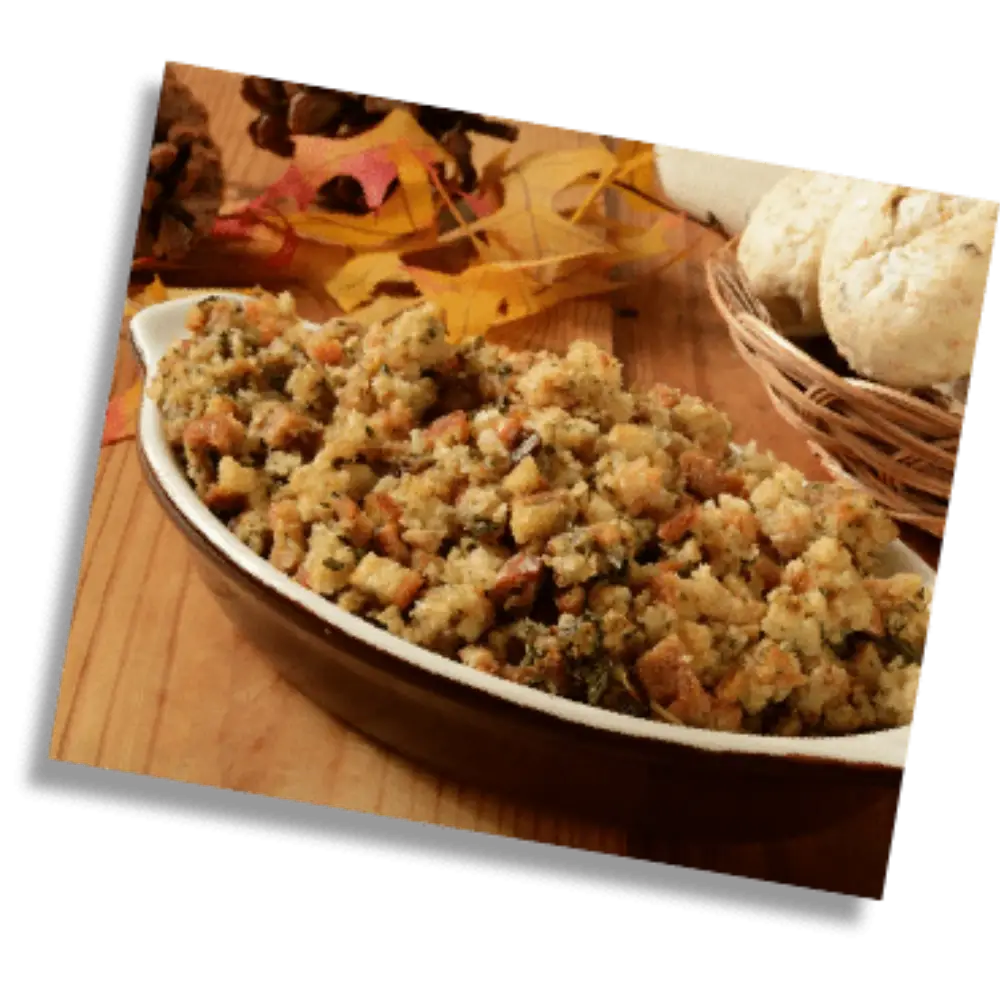 Homemade herb stuffing served in a white dish with bread rolls and autumn leaves in the background.