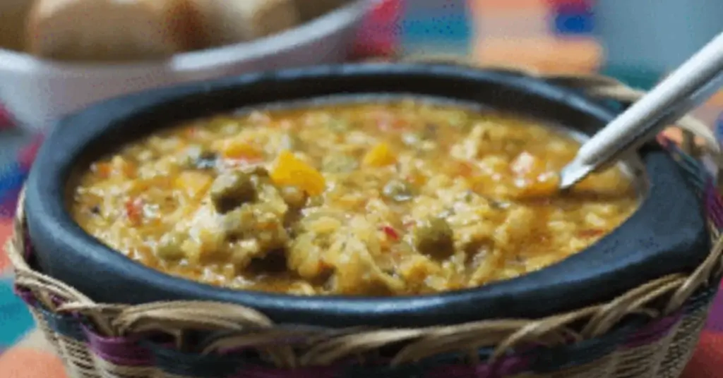 Bowl of spiced vegetable dip or curry with a spoon, served in a woven basket with colourful fabric in the background.