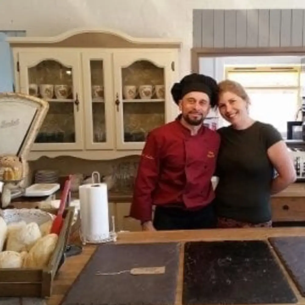Two people standing behind the counter inside Yare Valley Farm Shop, with bread and shop displays around them.