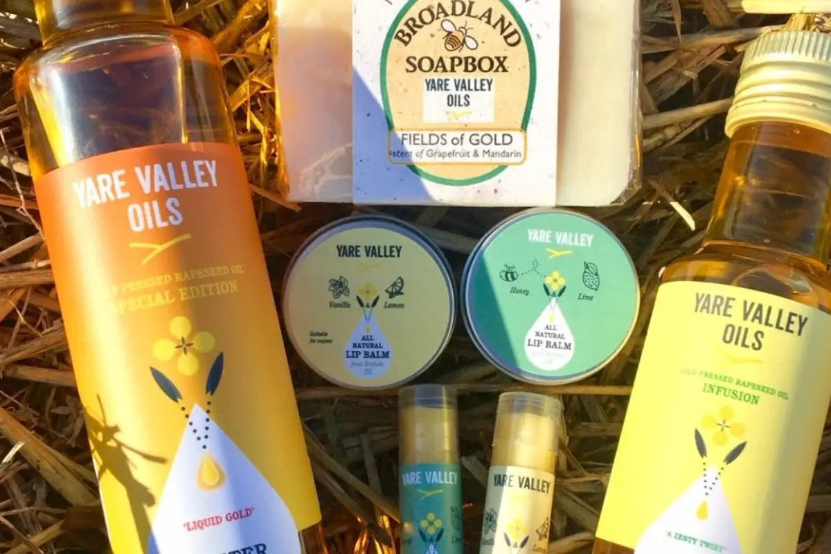 Yare Valley Oils products displayed on straw, including rapeseed oil bottles, soap, lip balms and small gift items.