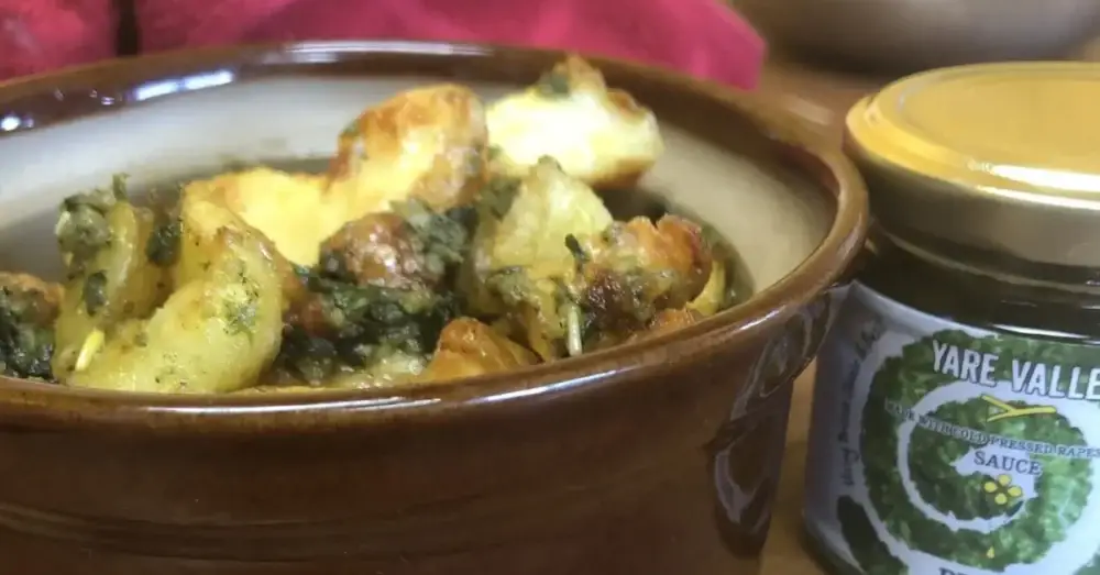Roasted potatoes served in a bowl beside a jar of Yare Valley sauce