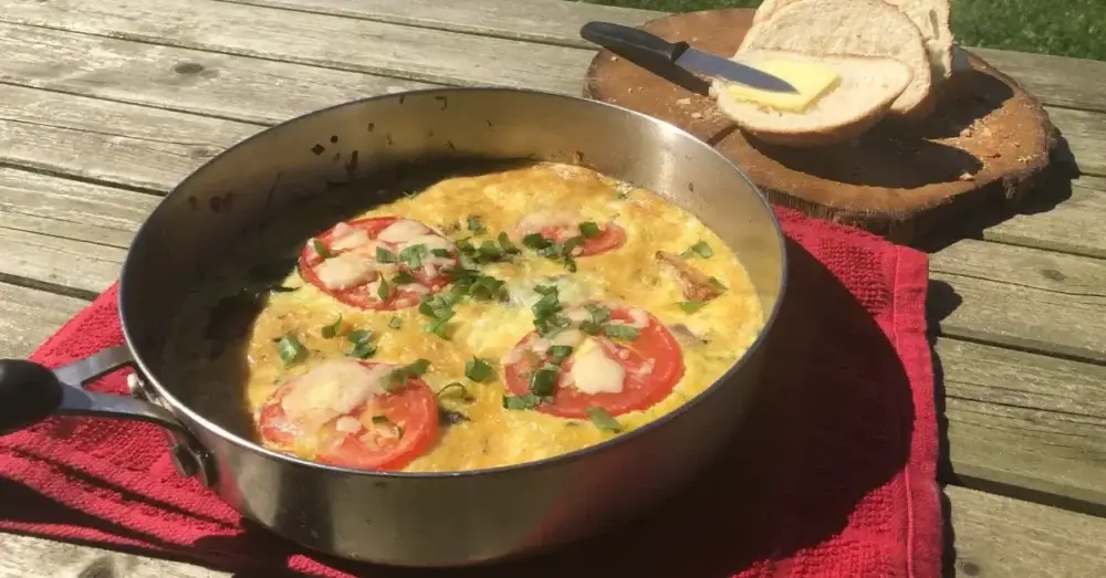 Fresh tomato and herb frittata cooked in a pan on an outdoor wooden table