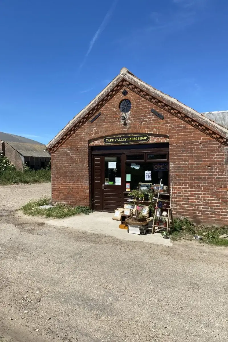 Traditional brick farm shop entrance at Yare Valley with outdoor produce displays and surrounding farm buildings.