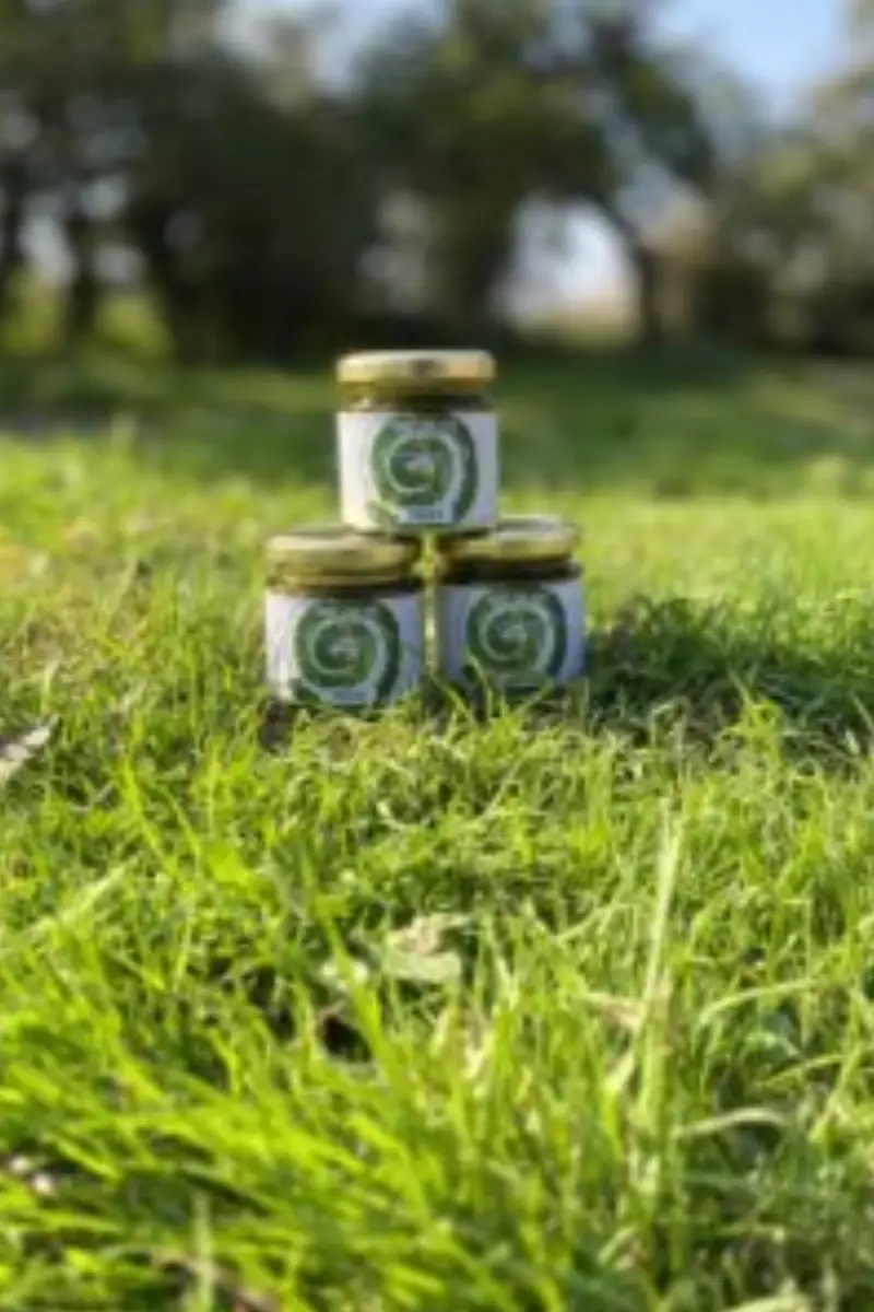 Small jars of Yare Valley condiments stacked on grass outdoors, with a blurred countryside background.