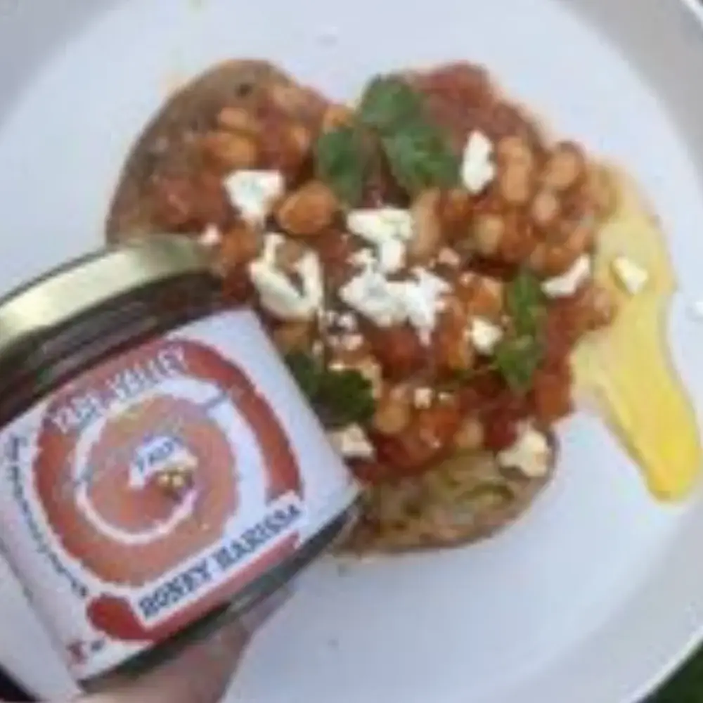 Yare Valley Honey Harissa paste held beside beans on toast with crumbled cheese, parsley and rapeseed oil.