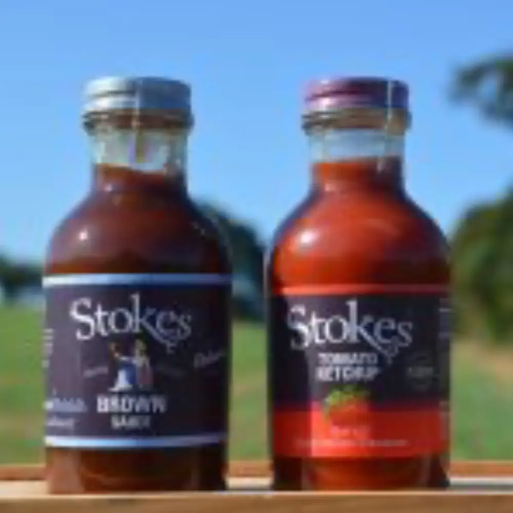 Stokes brown sauce and tomato ketchup bottles displayed outdoors with Yare Valley countryside in the background.