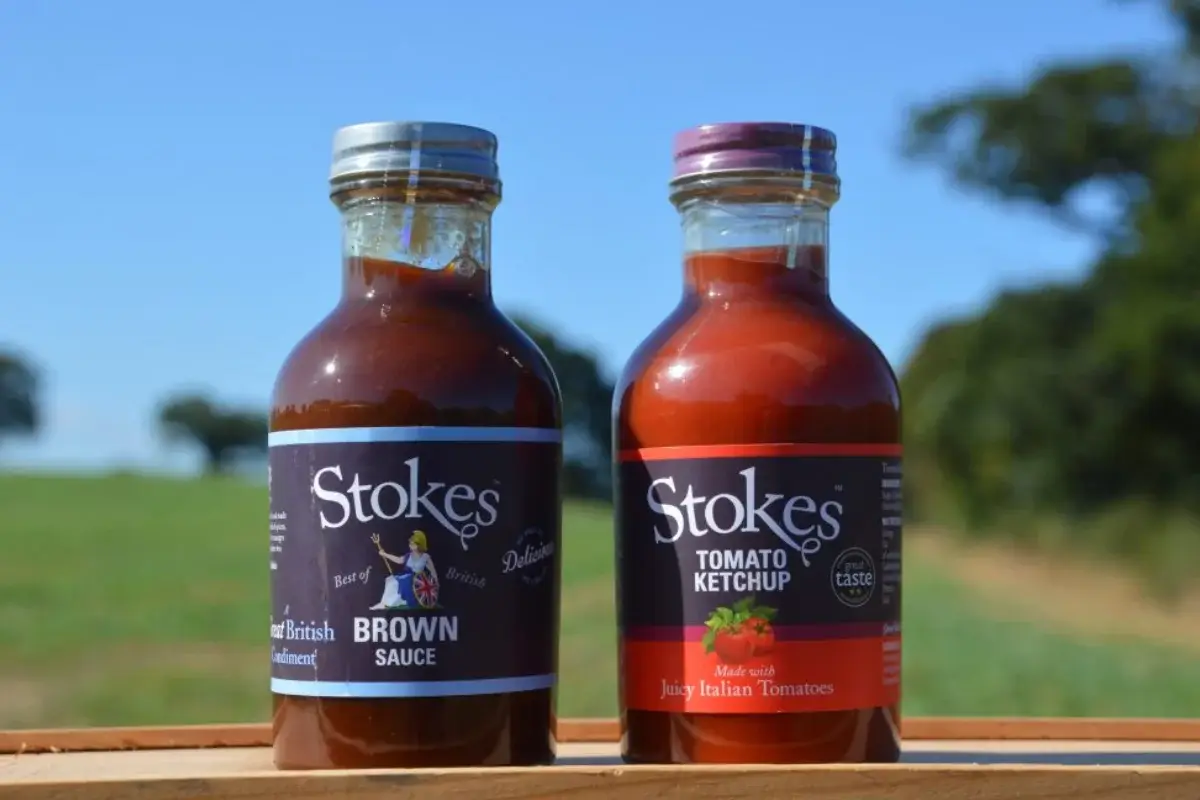 Stokes brown sauce and tomato ketchup bottles displayed outdoors on a wooden tray at Yare Valley Farm Shop.