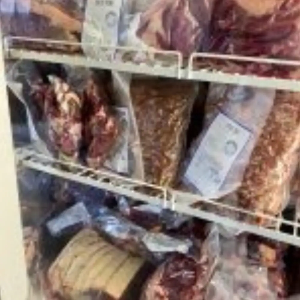 Assorted farm shop meats and joints packed for sale in a chilled display cabinet.