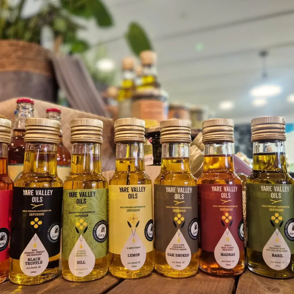 Yare Valley infused oils selection in glass bottles on wooden display featuring flavours like dill, lemon, chilli, marjoram and basil