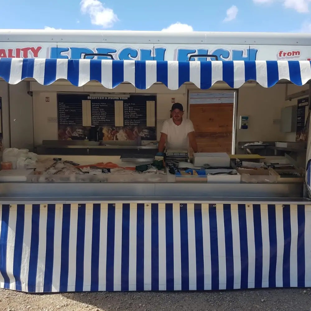 Traditional fish stall with blue and white striped canopy selling fresh fish at a market.