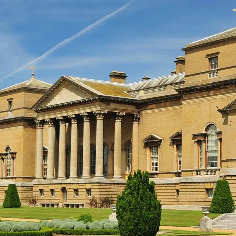 Historic country estate building with columned entrance, formal gardens and blue sky