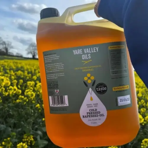 Large bottle of Yare Valley Oils cold pressed rapeseed oil held in front of a yellow oilseed rape field