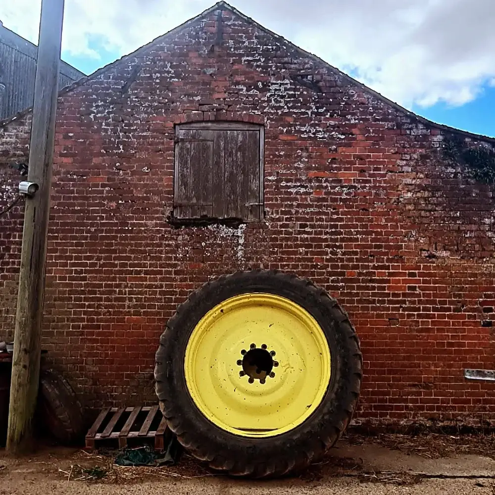 Large tractor wheel leaning against an old red brick farm building